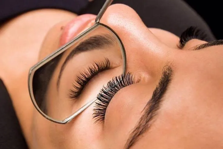 Primer plano de extensiones de pestañas profesionales y cejas perfiladas reflejadas en espejo metálico de lashmaker.
