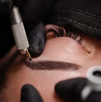 Especialista realizando tratamiento de microblading de cejas con un inductor manual (tebori).
