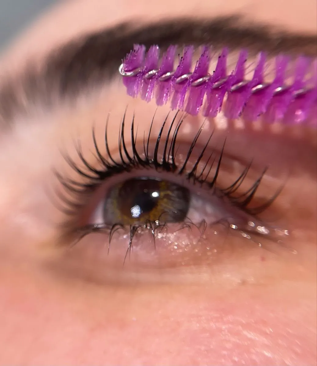 Ojo de cliente mostrando pestañas naturales levantadas y definidas siendo peinadas por un cepillo morado.